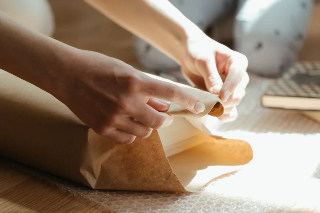 Hände wickeln ein Geschenk in braunes Packpapier, Sonnenlicht von der Seite